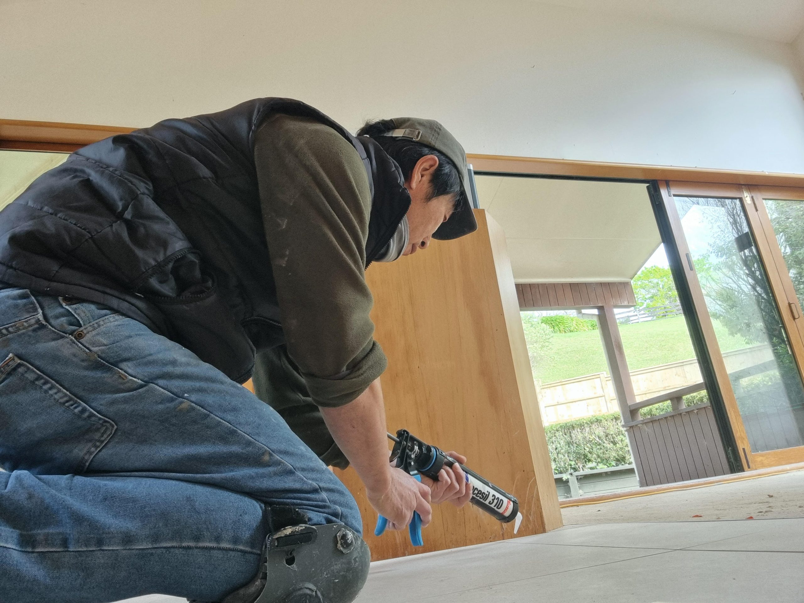 Auckland tiling and re-siliconing specialist applying sealant to floor tiles with a caulking gun – professional regrouting services for durable results.